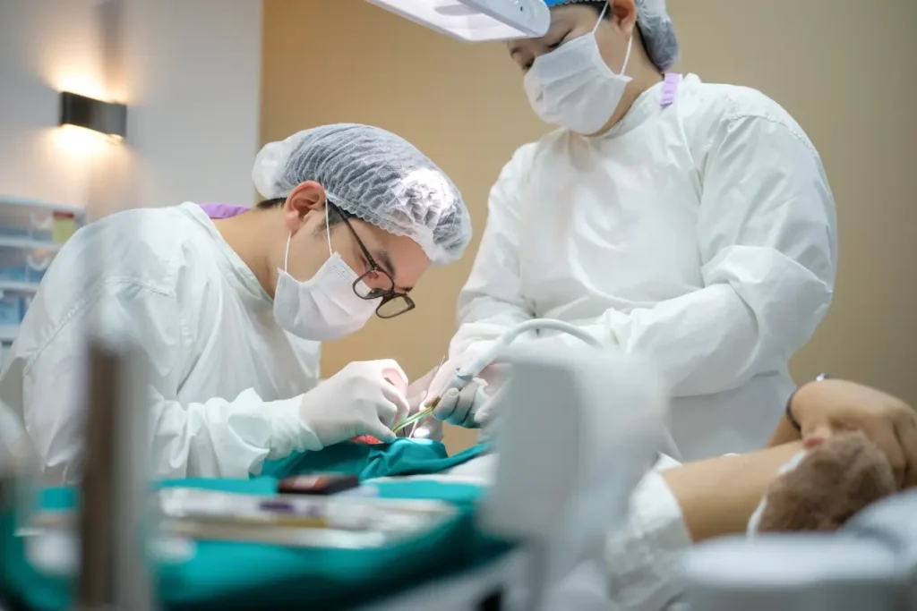 A dentist and her assistant gathers around a patient, performing a procedure.